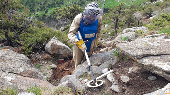 A deminer using their metal detector above rocks and soil