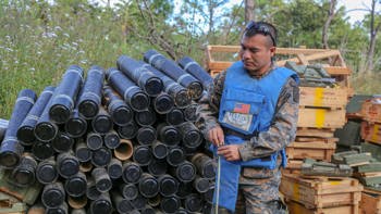 A deminer stands in front of crates and cylinder containers outside