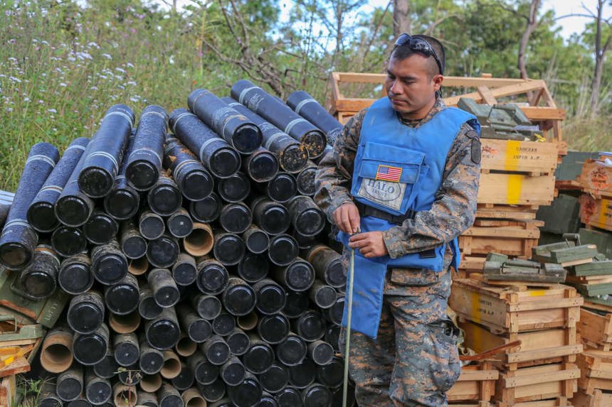 A deminer stands in front of crates and cylinder containers outside