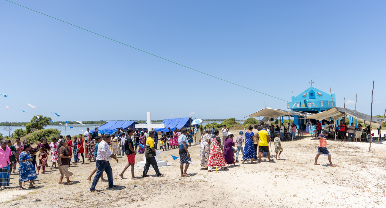 Parishioners walk across the sandy land in front of the bright blue church