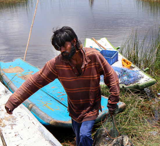 A man drags a net full of fish along the shore of a lagoon.