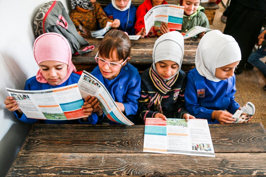Young girls in Syria read explosive ordnance risk education materials in a classroom