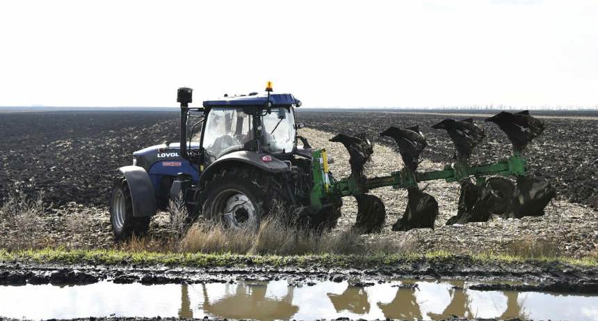 A large tractor sits parked on the side of a farm field