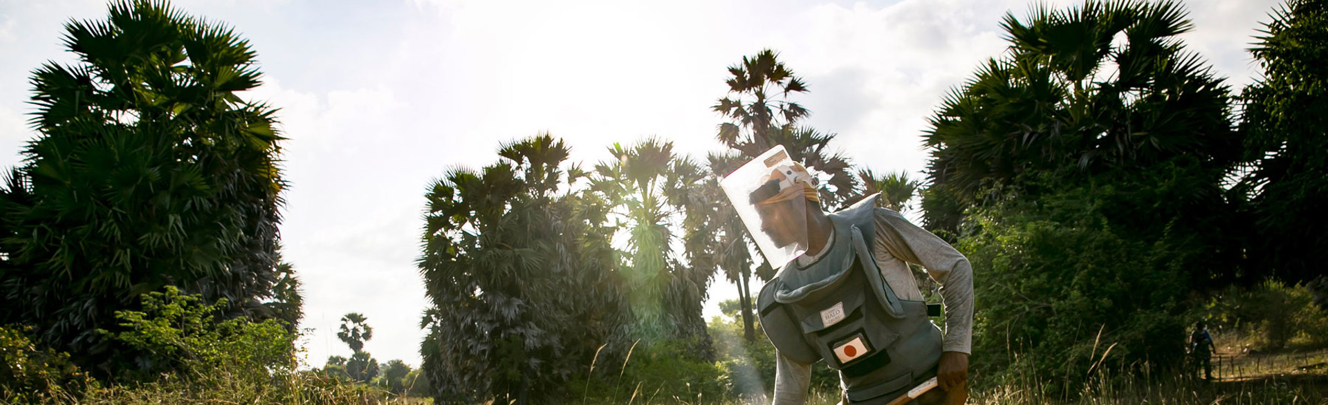 A deminer wearing PPE rakes the soil