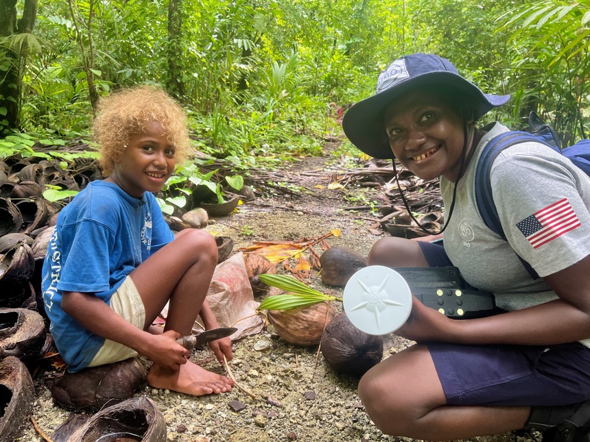 A HALO survey specialist poses in the forest with young girl harvesting coconuts