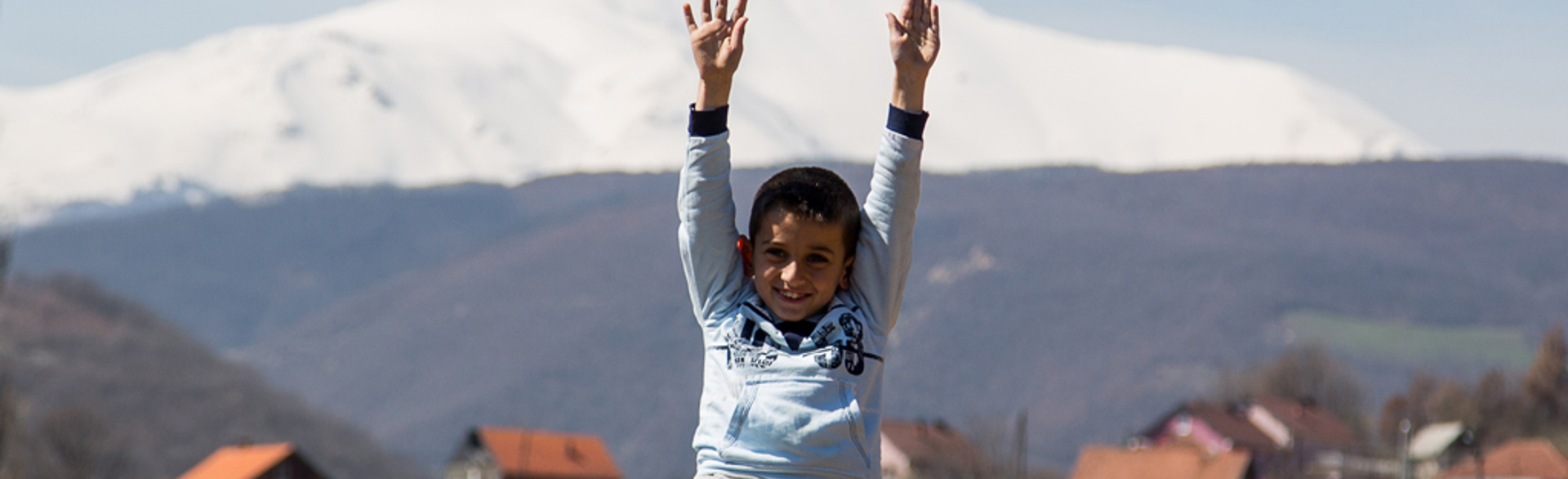 A child smiling in front of houses and a mountain