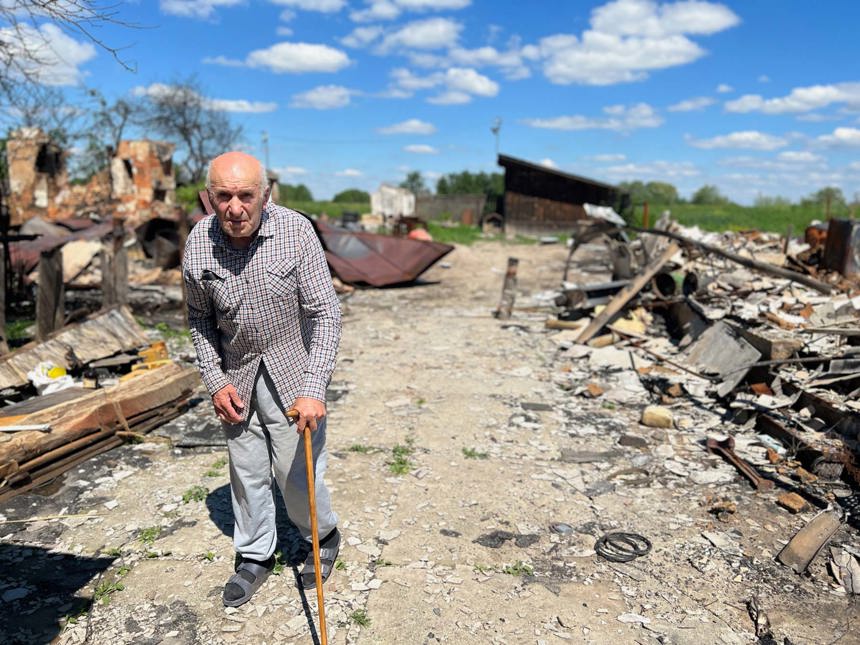 An elderly man stands with his walking stick amongst the rubble in Ukraine