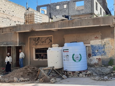 Three people stand in front of the rubble of a home in Taiz, Yemen.